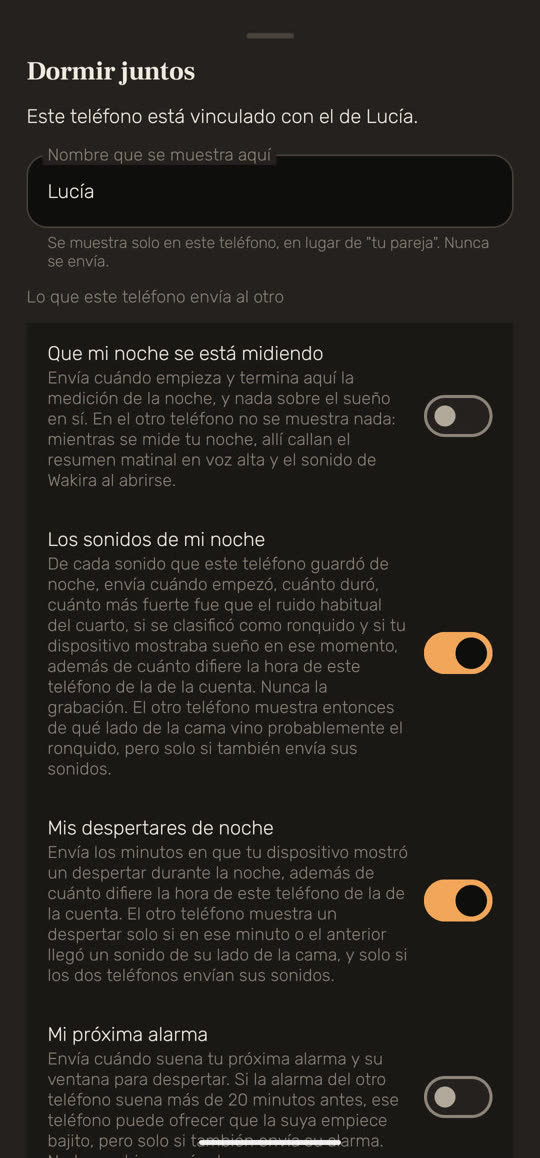Pantalla de Wakira, con datos de ejemplo: «Dormir juntos», con «Este teléfono está vinculado con el de Lucía.» y un campo de nombre que dice «Lucía». Debajo, «Lo que este teléfono envía al otro» y cuatro interruptores, cada uno con su explicación: «Que mi noche se está midiendo» está apagado, «Los sonidos de mi noche» encendido, «Mis despertares de noche» encendido y «Mi próxima alarma» apagado.